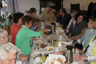 Viele Menschen sitzen gemeinsam beim Frühstück an einem langen Tisch.