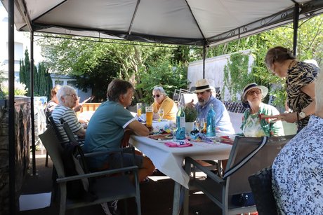 Mehrere Personen sitzen drau&szlig;en an einem langen Tisch und unterhalten sich miteinander.
