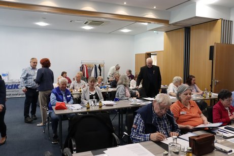 Menschen sitzen an Tischen in einem Saal.