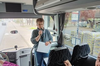 Eine Frau mit Mikrofon steht vorn im Reisebus und spricht.