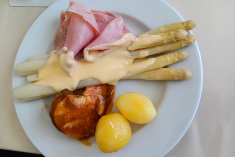 Man sieht einen Porzellanteller mit Spargelstangen, Kartoffeln, So&szlig;e und ein Schweinemedaillon