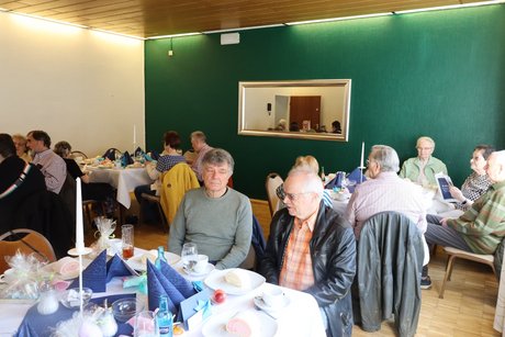 An mehreren Tischen sitzen Menschen und unterhalten sich.