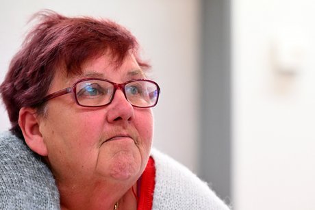 Eine Frau mit dunkelrotem Kurzhaarschnitt und roter Brille schaut rechts aus dem Bild heraus