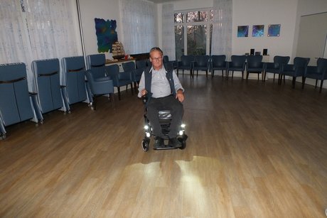 Ein Mann f&auml;hrt mit einem Elektrorollstuhl durch den Raum.