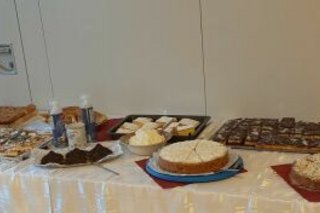 Ein langer Buffet-Tisch ist vollgestellt mit zahlreichen Kuchen und Torten. Rechts im Bild Stapel mit weißen Tellern.