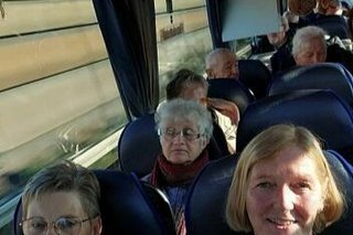 Menschen sitzen in einem Reisebus, dessen Gepäckablage mit Lichterketten und Weihnachtsgirlanden geschmückt ist.