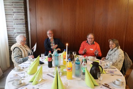 Vier Personen sitzen an einem gedeckten runden Tisch.