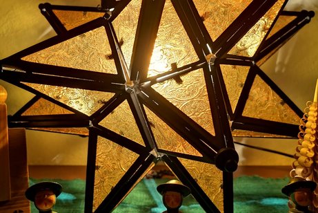 Zu sehen ist ein Herrenhuter Stern aus Metall und Glas in gelb und im Vordergrund ein paar Kurrendes&auml;nger aus Holz