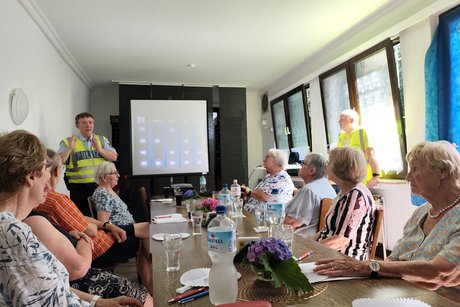 Verkehrsquiz mit Polizeihauptkommissar Hans-Joachim Ruhl. Mehrere Personen sitzen an einem langen Tisch und hören Polizeihauptkommissar Hans-Joachim Ruhl zu.