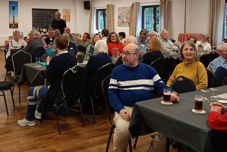 Auf dem Bild sieht man viele Personen sitzend an den Tischen. Sie unterhalten sich und lauchen der Musik. Es ist eine sch&ouml;ne Stimmung auf dem Bild. Es stehen Getr&auml;nke auf dem Tisch.