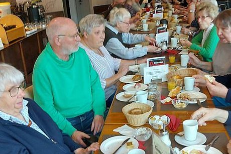 Viele Menschen sitzen gemeinsam beim Frühstück an einem langen Tisch.