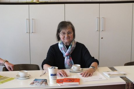 Eine Frau sitz an einem Tisch mit Unterlagen und Getr&auml;nken.