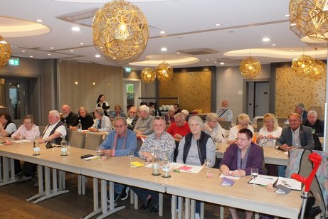 Die Mitglieder sitzen an langen Tischen in drei Reihen hintereinander.