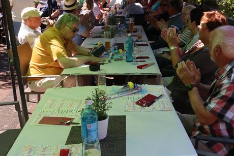 Menschen sitzen im Au&szlig;enbereich an langen Tischen.