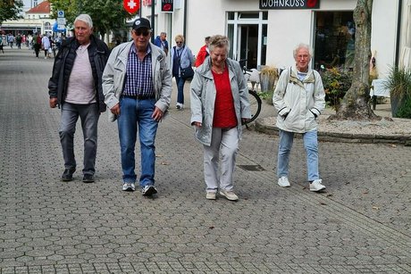 Zwei Männer und zwei Frauen laufen nebeneinander über eine gepflasterte Straße.