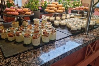 Platten mit Donuts und zahlreiche kleine Gläschen mit verschiedenen Desserts sind auf einem Buffet angerichtet.