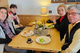 Drei Frauen und ein Mann sitzen gemeinsam an einem Tisch. Auf dem Tisch benutztes Essgeschirr.