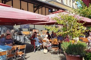 Männer und Frauenn sitzen unter großen Sonnenschirmen im Biergarten des Brauhauses "Alter Bahnhof"