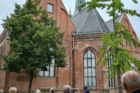 Menschen stehen auf einem Platz vor einer Kirche aus roten Ziegeln.