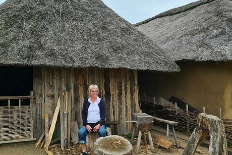 Eine Frau sitzt auf einem Baumstumpf vor einem der reetgedeckten Wikingerhäuschen in Haithabu.