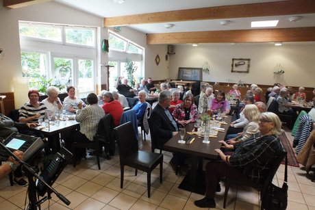 Viele Menschen sitzen an mehreren langen Tischen.
