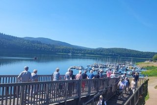 Der Steg, der im Zickzack zum Bootsanleger führt aus einer anderen Perspektive fotografiert. Eine Gruppe Menschen ist darauf unterwegs.