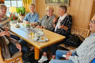 Eine Gruppe Männer und Frauen sitzen gemeinsam bei Getränken an einem Tisch.