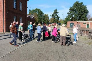 Eine Gruppe Menschen steht auf einem gepflasterten Platz vor dem roten Ziegelbau des Textilmuseums in Bocholt.