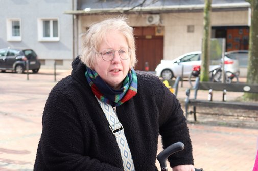 Eine Frau mit blondem Kurzhaarschnitt und Brille steht mit ihrem Rollator am VdK-Stand