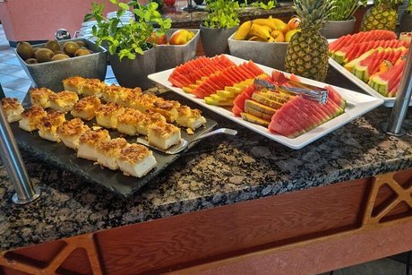 Zahlreiche kleine Kuchen und eine Platte mit Melonen und anderem Obst sind auf einem Buffet angerichtet.
