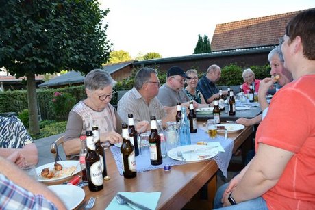 Menschen sitzen gemeinsam draußen an einer langen Tafel und essen.