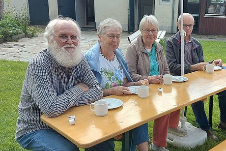 Zwei Männer und zwei Frauen sitzen nebeneinander an einem Biertisch und haben Kaffee und leere Kuchenteller vor sich stehen.