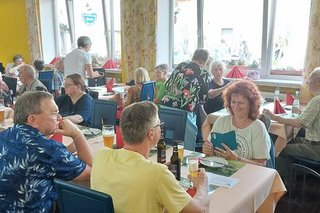 Menschen sitzen gemeinsam an Tischen im Restaurant der Straußenfarm.