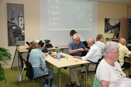 Menschen sitzen am Tisch h&ouml;ren den Vortrag zu
