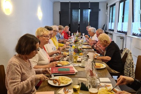 Mitgliedertreffen Mehrere Menschen sitzen an einem langen Tisch und speisen.