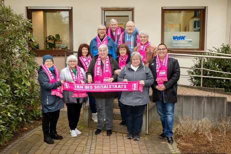 Frauen und Männer aus dem VdK Leverkusen mit rosa Fanschals "Ja zum Sozialstaat" vor der Geschäftsstelle in Leverkusen