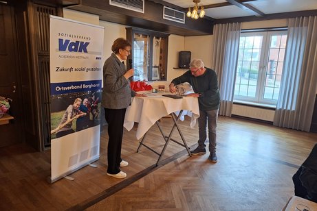 Jutta Baumhold und Dieter Strickmann stehen vorne am Stehtisch und ziehen die Bingo Kugeln.