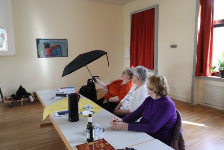 3 Frauen sitzen nebeneinander und probieren gerade die Funktion eines Schirmmodells aus.