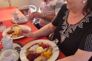 Eine Frau und ein Mann sitzen an einem eingedeckten Tisch mit Waffeln, Eis und Kirschen vor sich auf den Tellern.