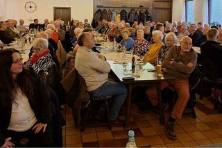 Viele Menschen sitzen an langen Tischreihen in einem Saal