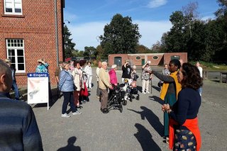 Eine Gruppe Menschen steht auf einem gepflasterten Platz vor dem roten Ziegelbau des Textilmuseums in Bocholt.