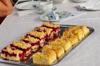 ein Tablett mit verschiedenen Kuchenstücken und ein Tablett mit belegten Brötchen an einem gedeckten Tisch