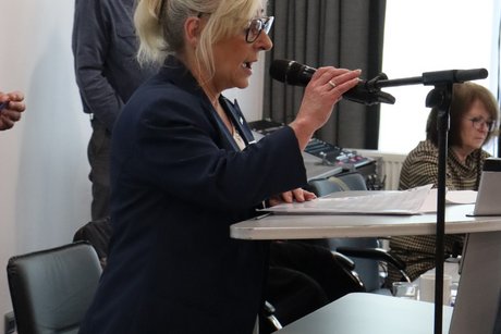 Eine Frau steht am Rednerpult und liest etwas vor.