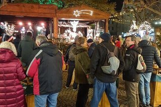 Besucher drängen sich um die Stehtische, die zwischen den weihnachtlich beleuchteten Buden auf dem Kopfsteinpflaster-Platz aufgestellt sind.