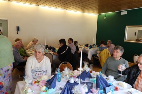 An mehreren gedeckten Tischen sitzen Menschen und unterhalten sich.