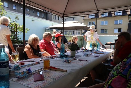 Mehrere Personen sitzen an einem langen Tisch auf der Terrasse.