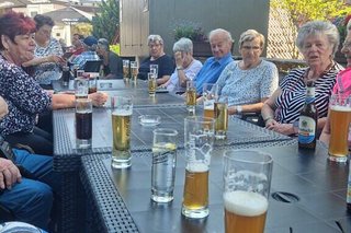 Eine Gruppe Menschen sitzt gemeinsam an einem langen Tisch und genießt kalte Getränke.