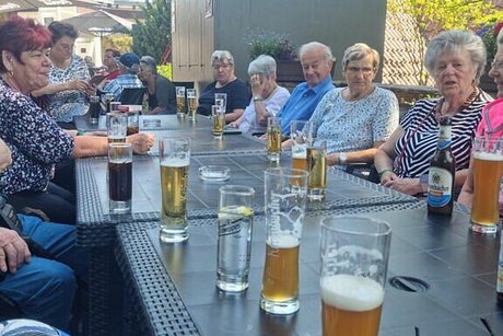 Eine Gruppe Menschen sitzt gemeinsam an einem langen Tisch und genießt kalte Getränke.