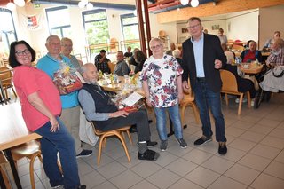 Gruppenfoto der Jubilare mit Präsentkörben. Im Hintergrund sitzen weitere Mitglieder des Ortsverbandes an Tischen.