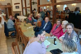 Menschen sitzen in einer Gaststube an einem langen Tisch.